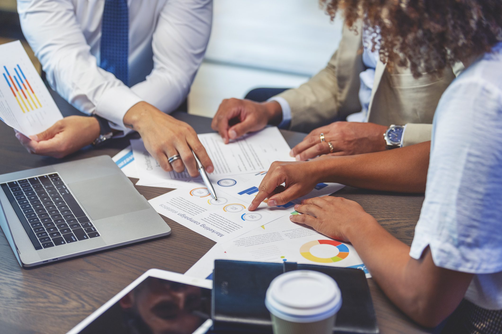 People pointing to financial graphs and data sheets next to a laptop