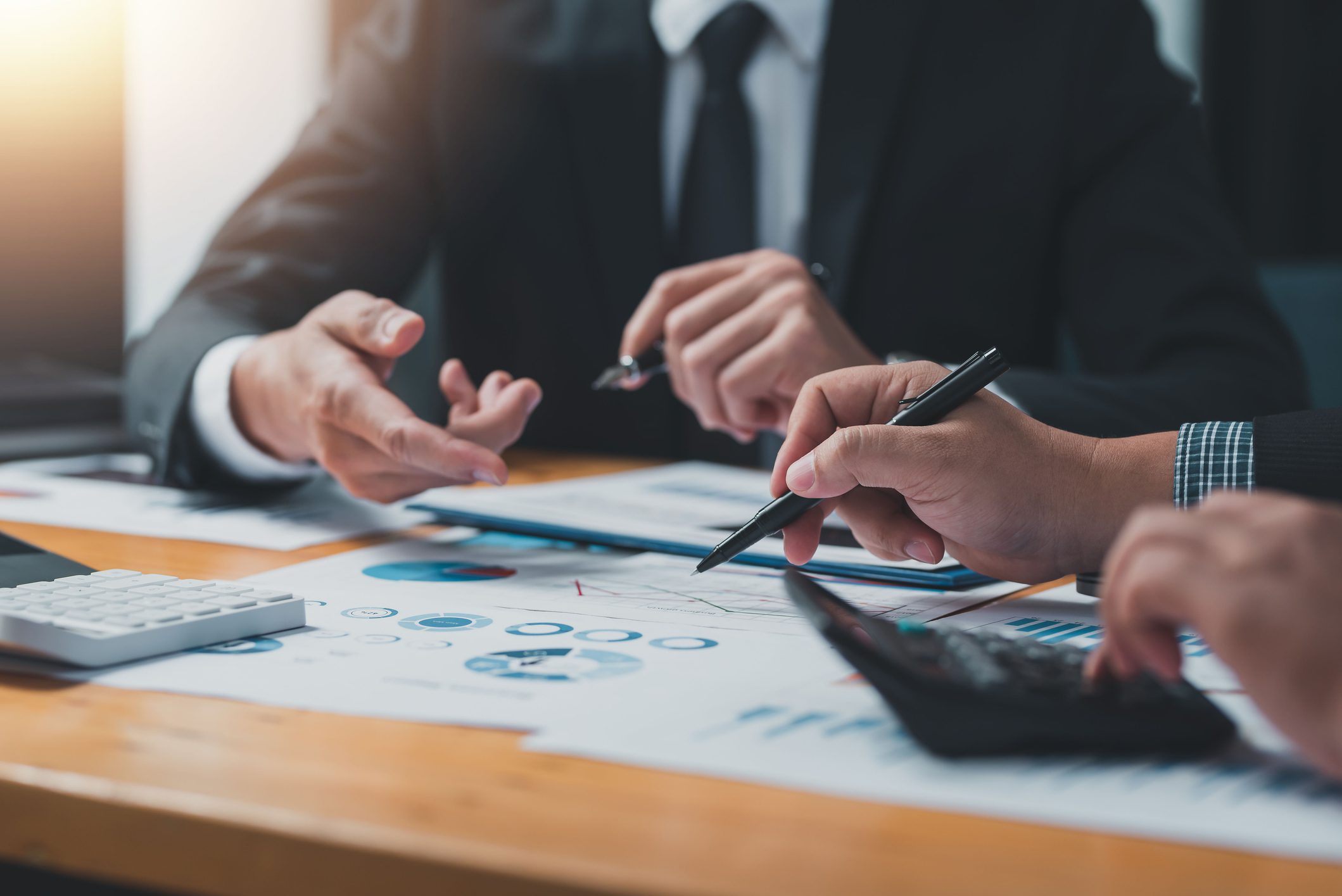 Two business professionals in suits reviewing financial charts with calculators and pens