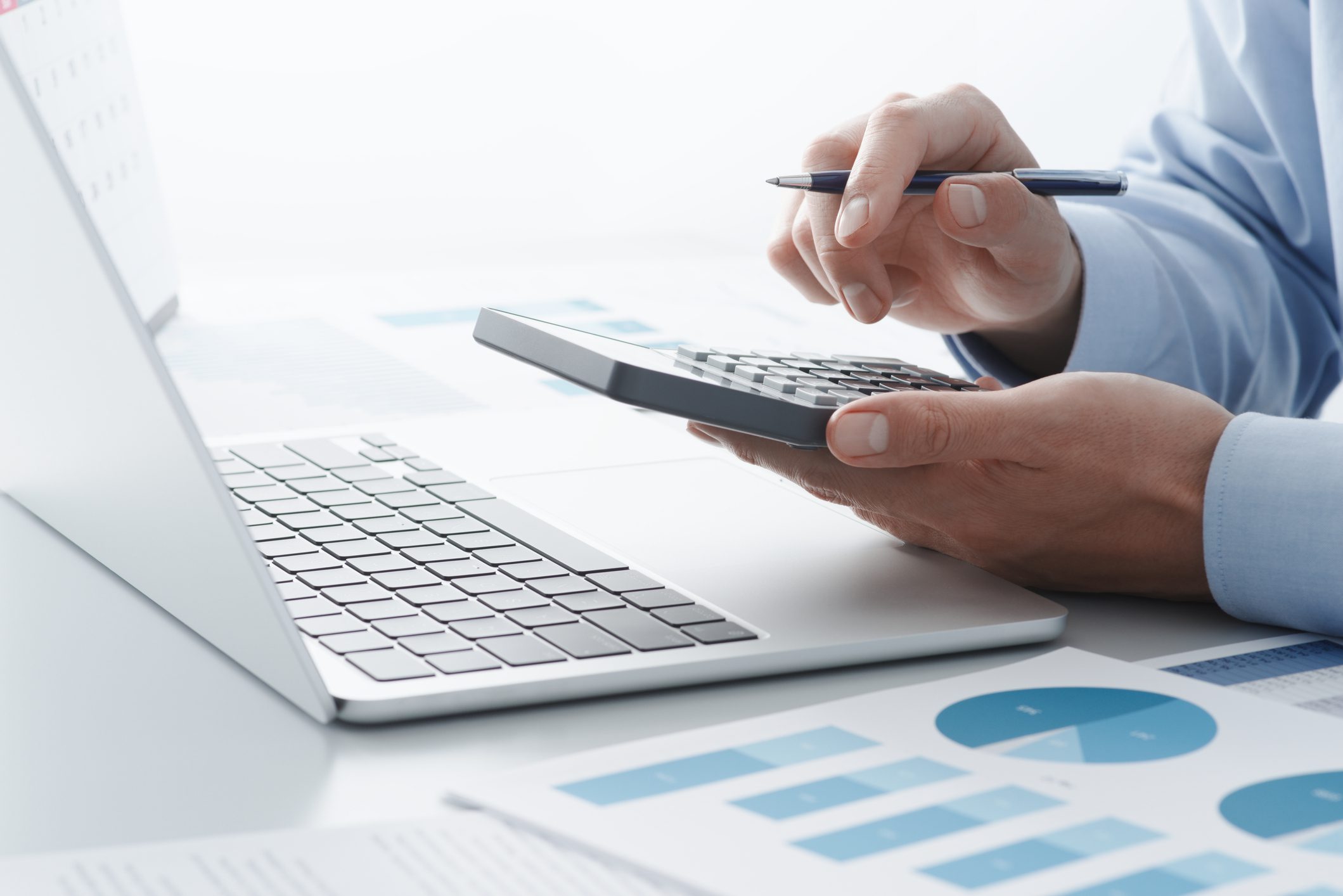 Hands using calculator with pen near laptop and financial charts on desk