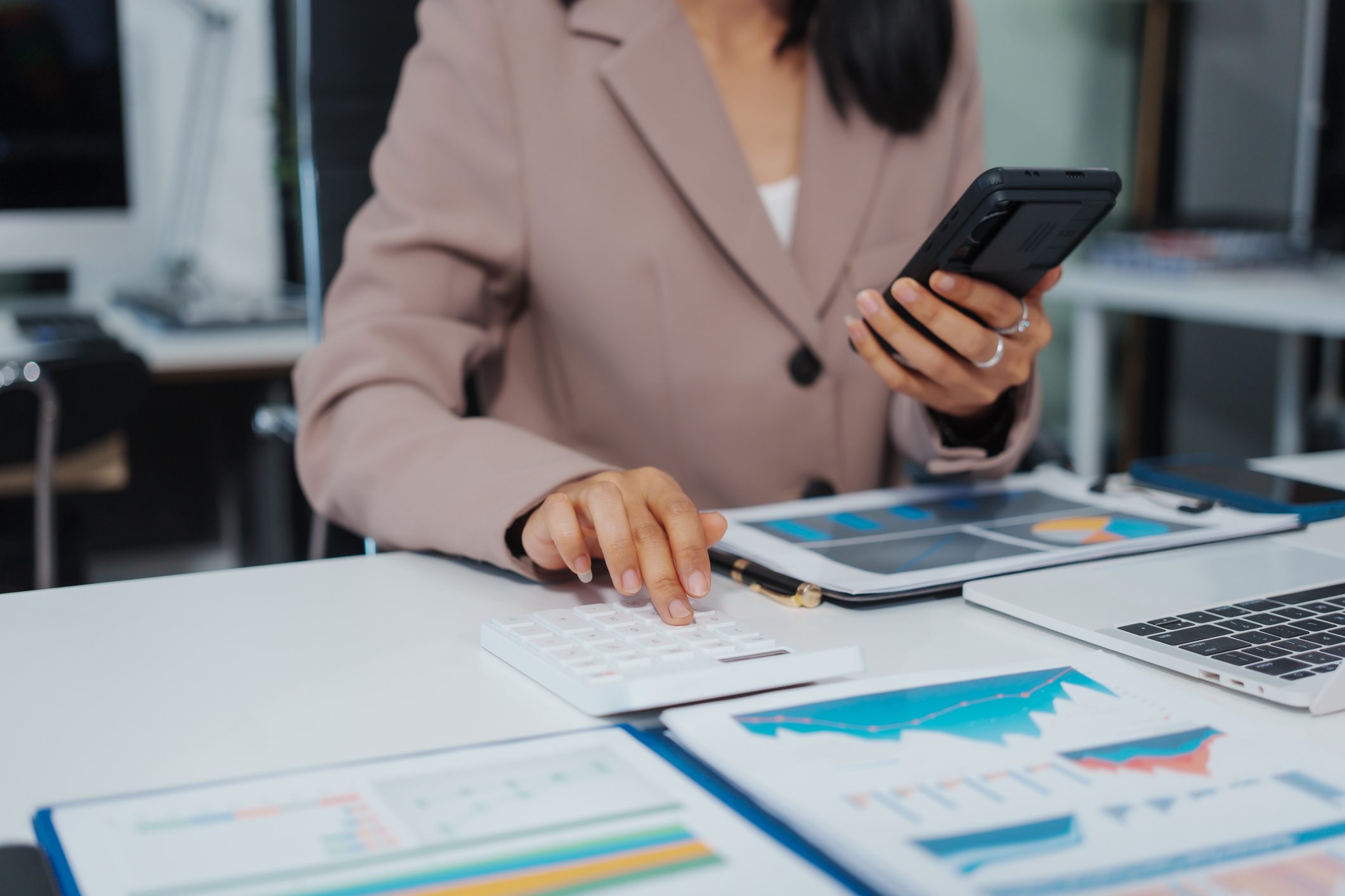 Businesswoman using calculator and smartphone with financial charts on desk