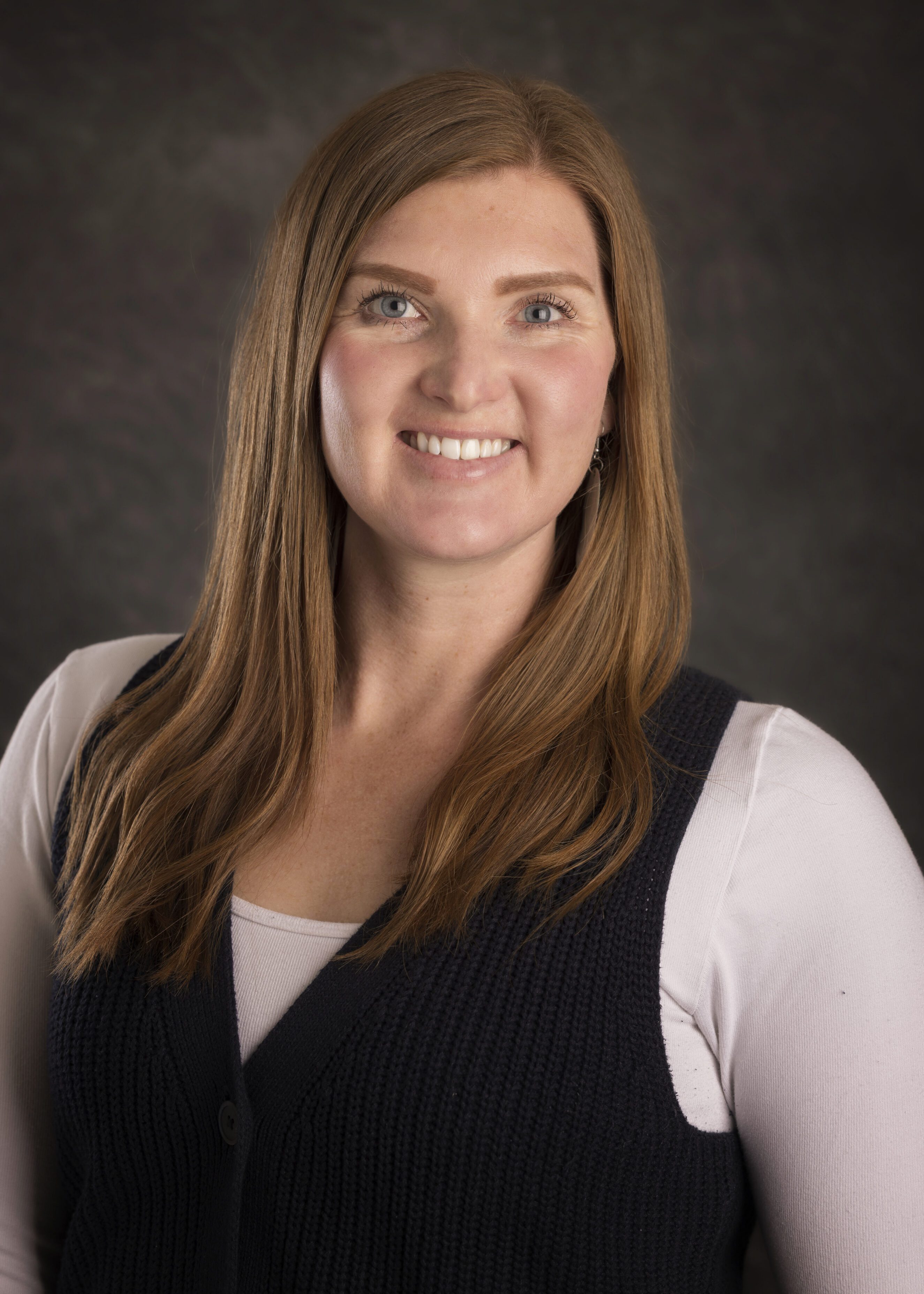 Smiling woman with long straight reddish hair wearing a black knit vest